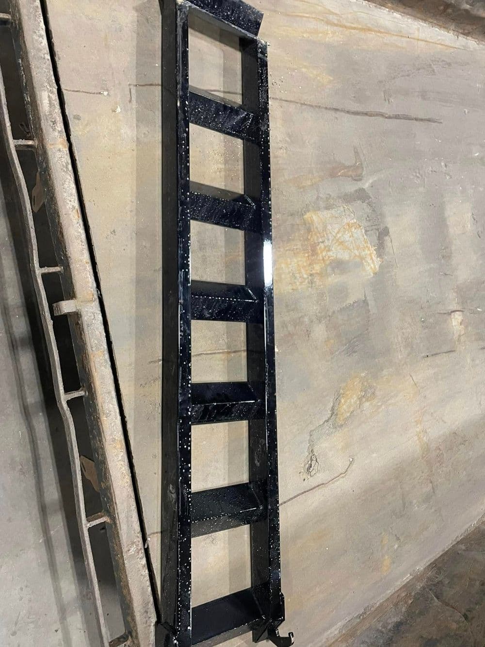 Black metal ladder resting on a concrete surface, showcasing five evenly spaced rungs.