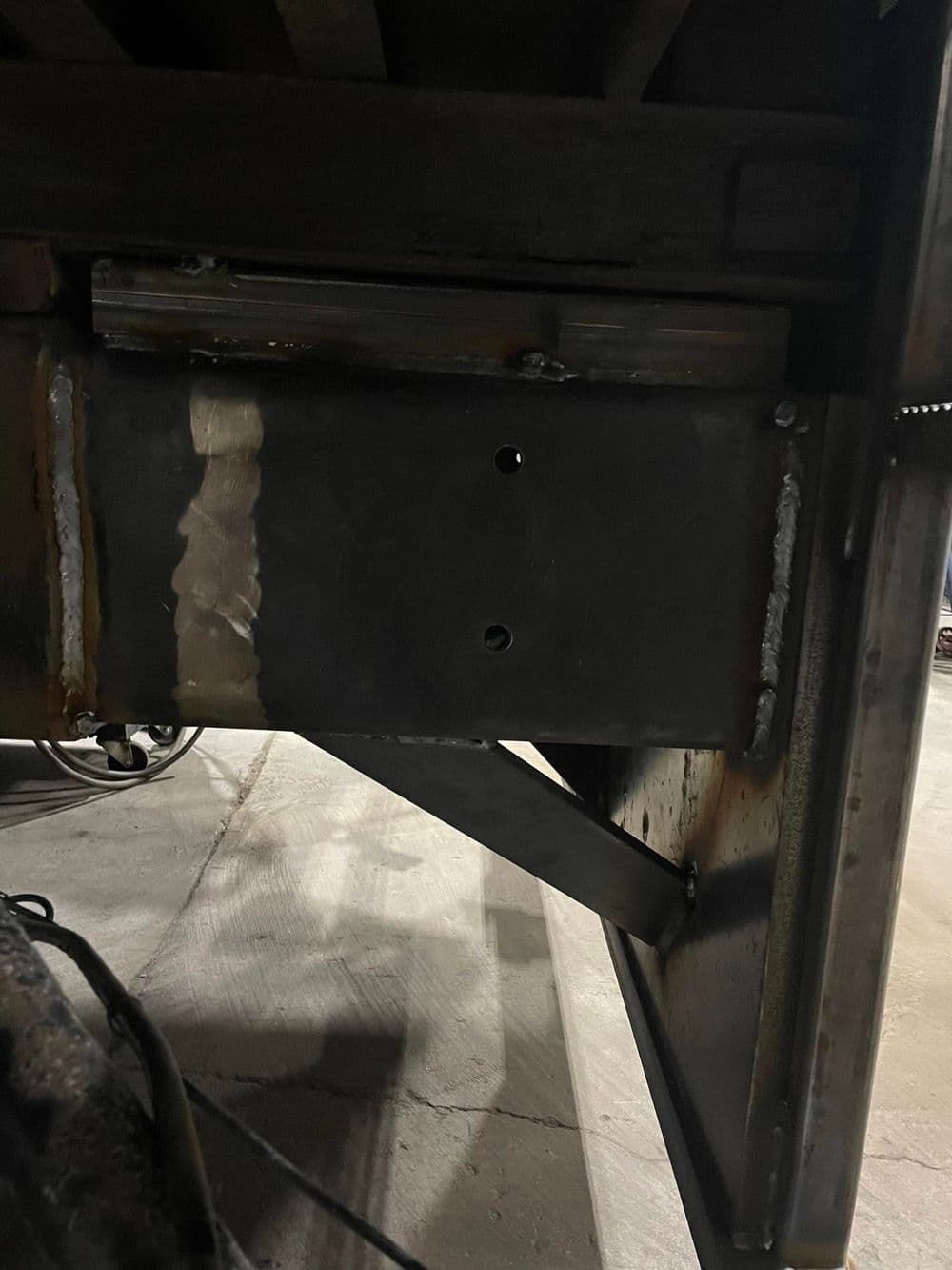 Welded metal bracket under a truck bed, showing visible seams and screw holes.