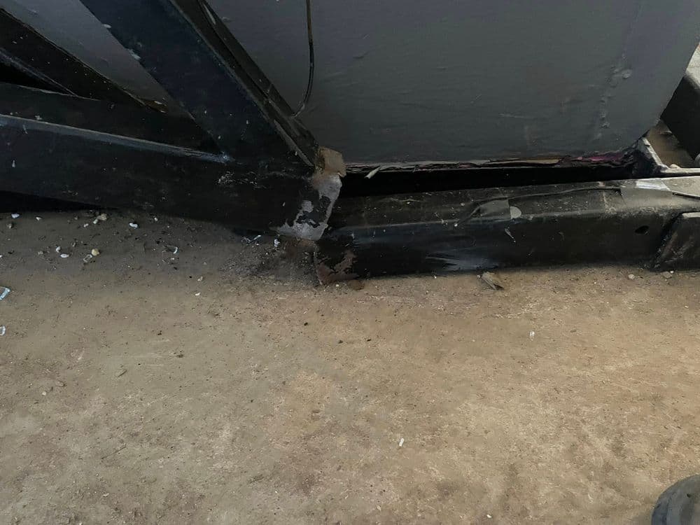 Close-up of damaged metal frame on a floor, showing rust and debris accumulation.