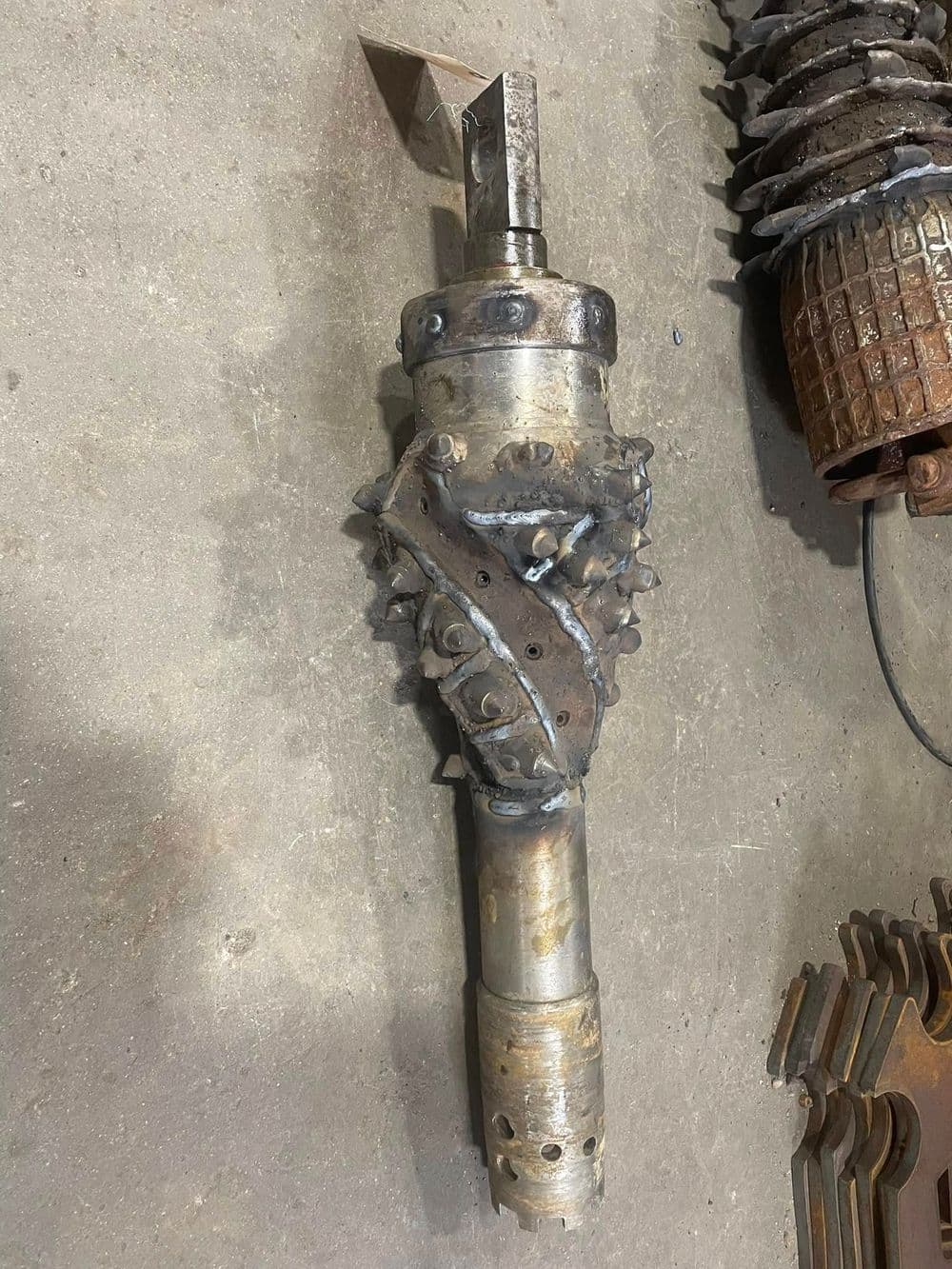 Industrial drilling tool with spiked design and metallic finish on a workshop floor.