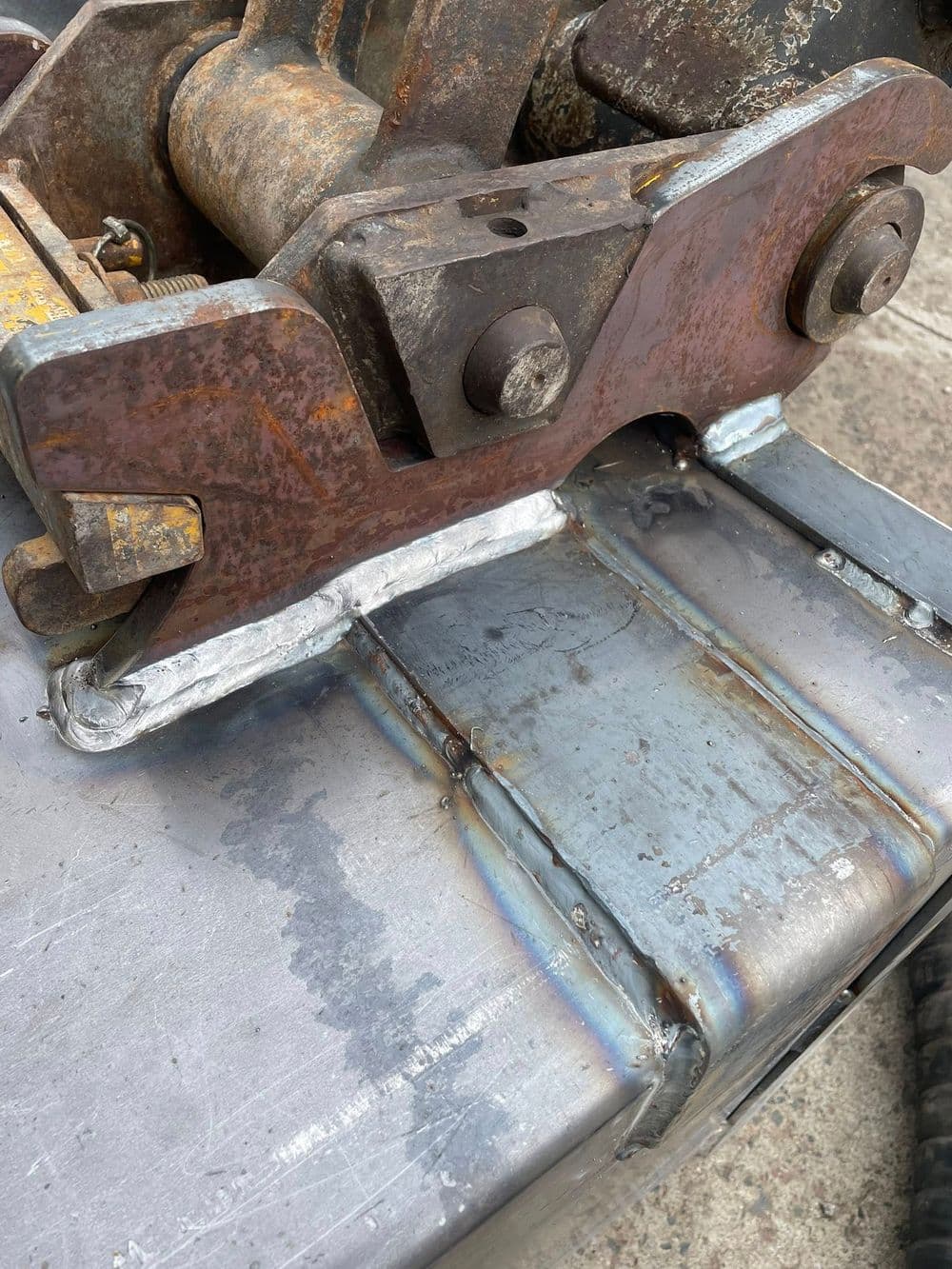 Close-up of welded metal joint on heavy machinery with rusted and polished steel surfaces.