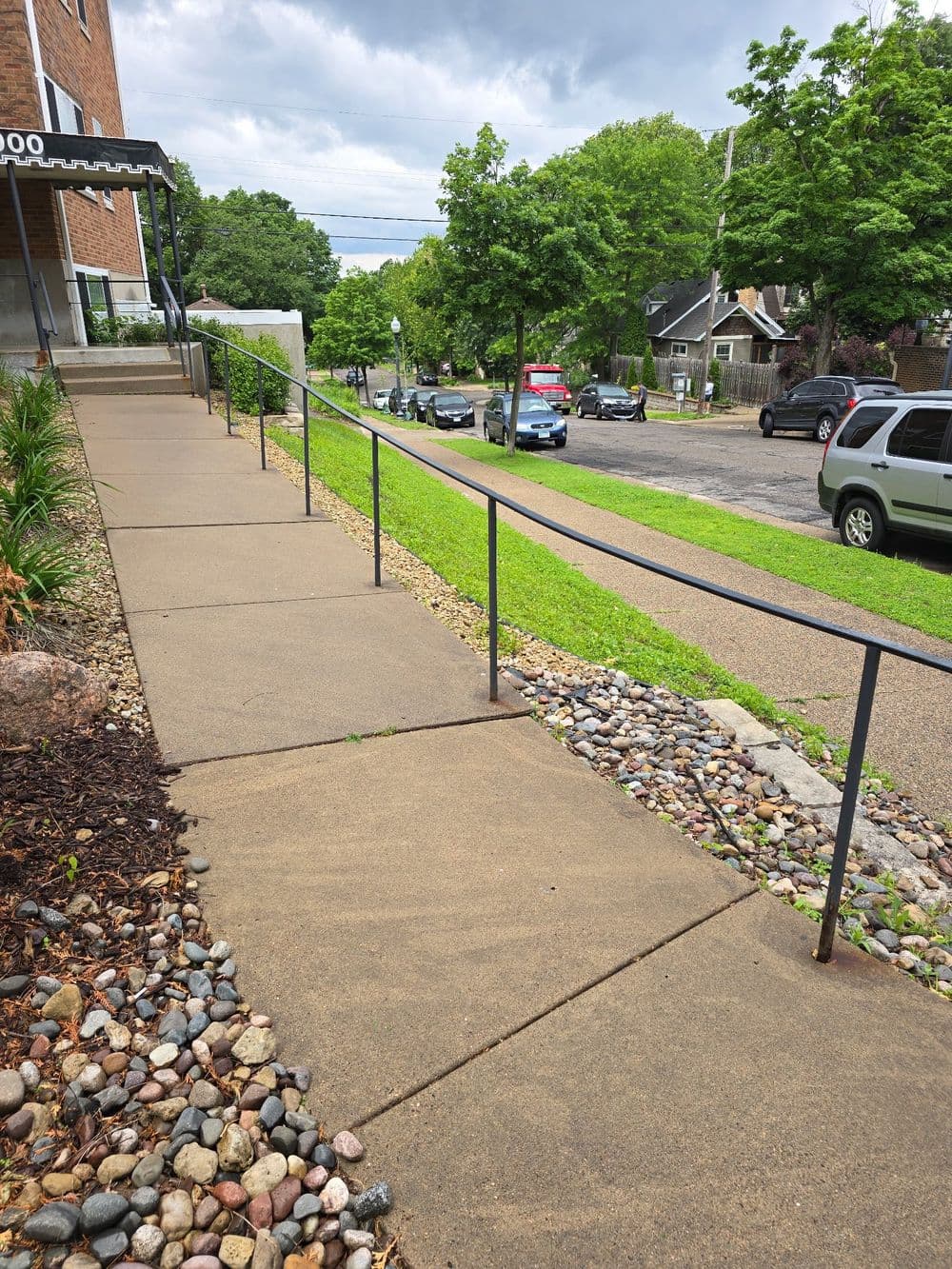 Accessible sidewalk with a railing, landscaped rocks, and street view of parked cars.