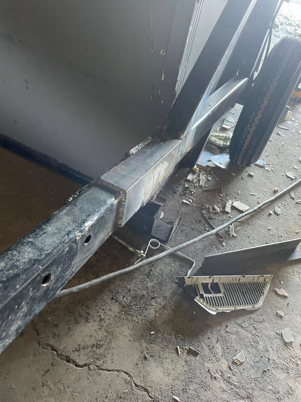 Close-up of a metal trailer frame showing welding details and nearby debris on the ground.