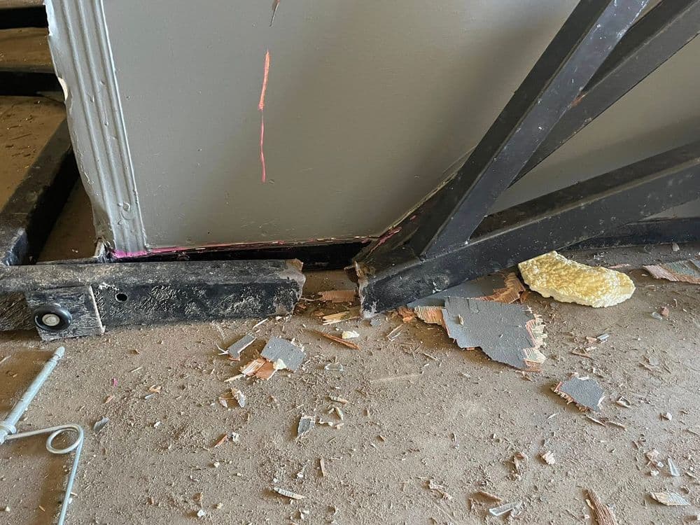 Damaged staircase corner with exposed wood, debris, and yellow foam insulation visible.
