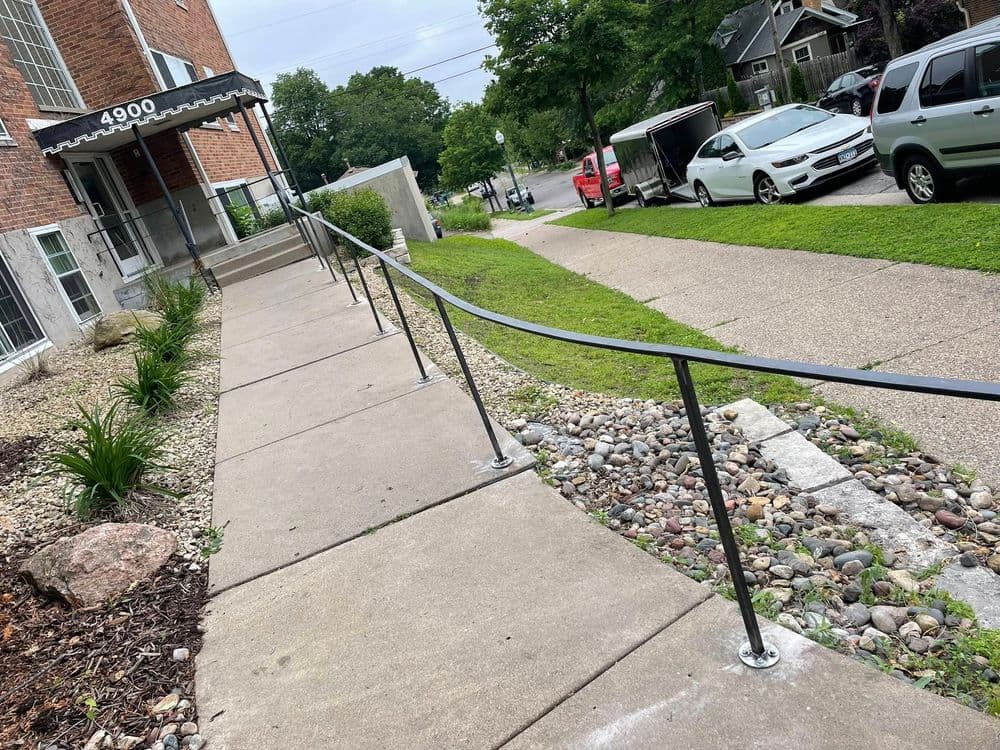 Accessible sidewalk with railing leading to a brick building entrance on a urban street.